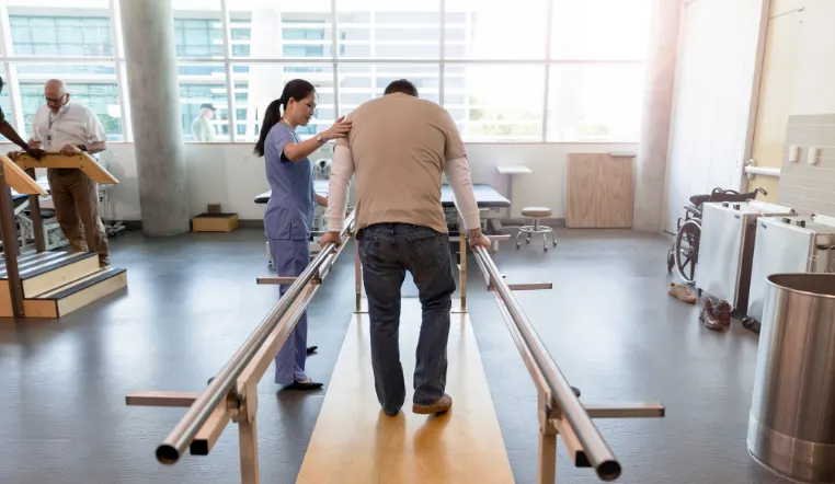 man using rehab equipment with help from nurse